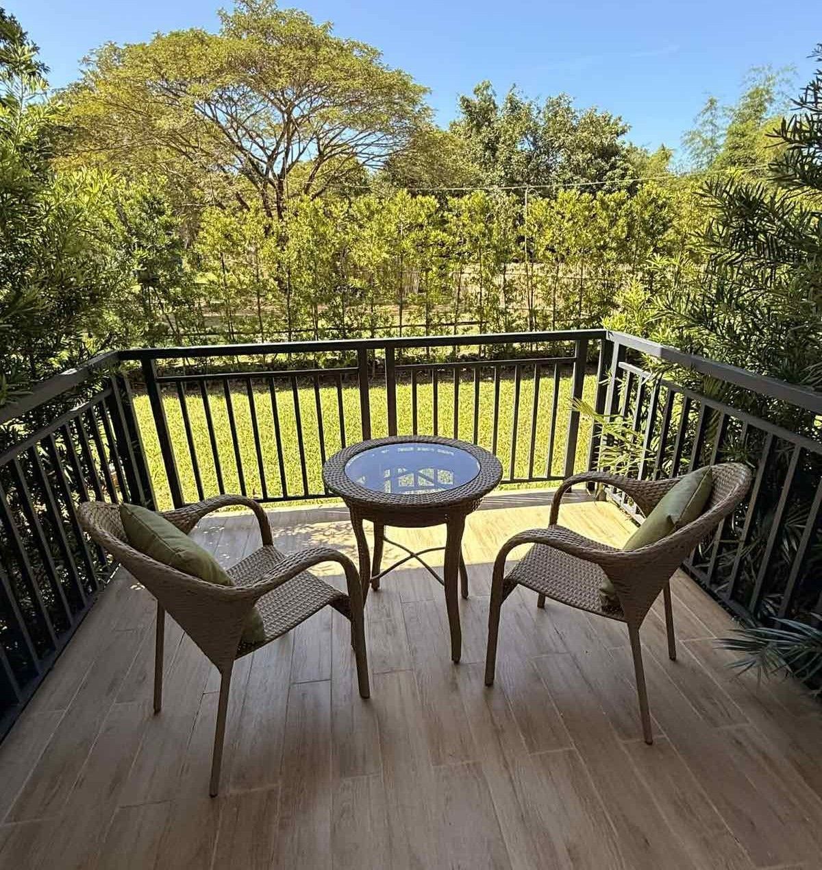 Balcony with two wicker chairs and a small round table overlooking a green yard and trees
