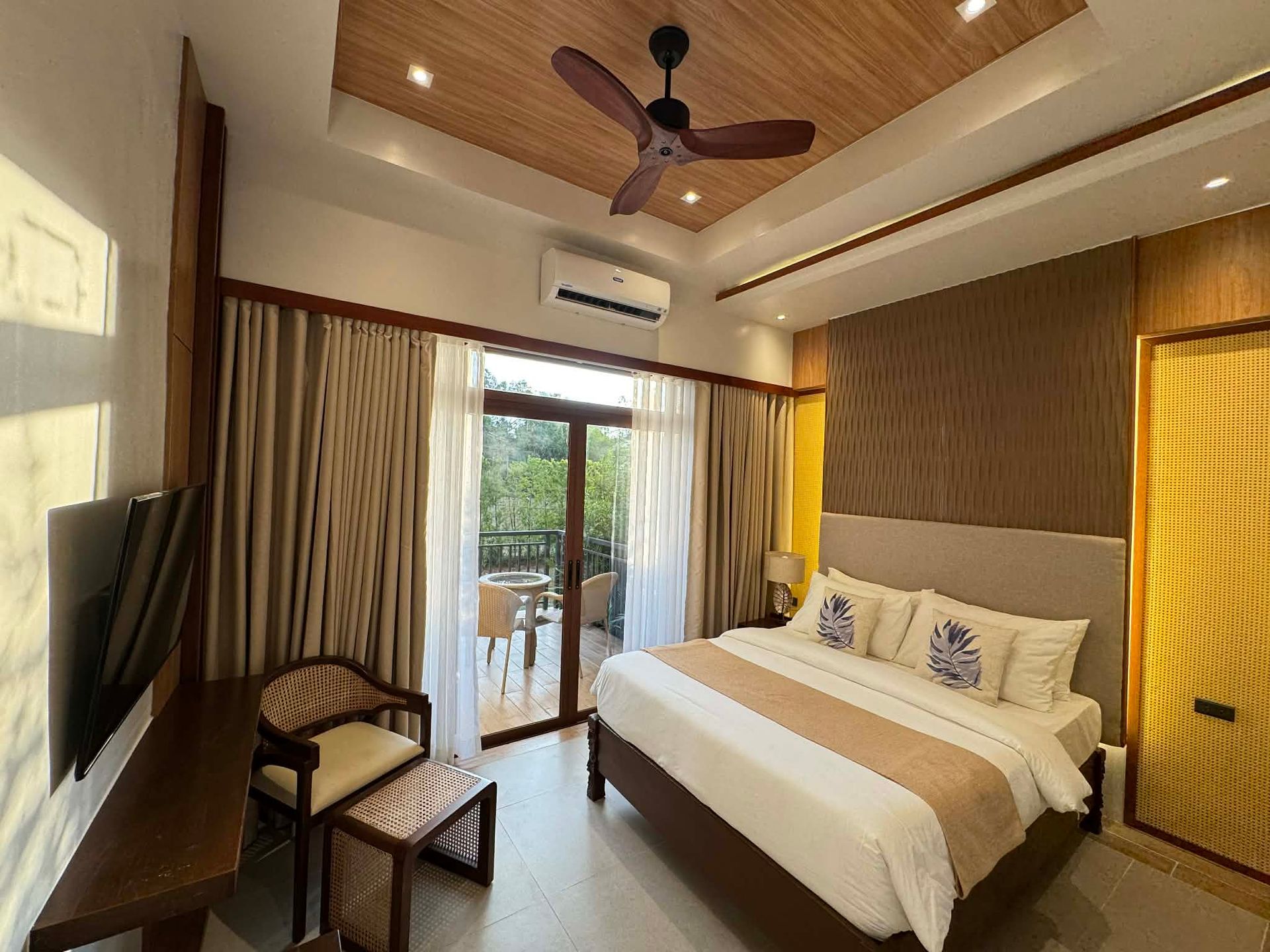 Bright bedroom with a bed, ceiling fan, wall TV, and sliding glass doors to a balcony.
