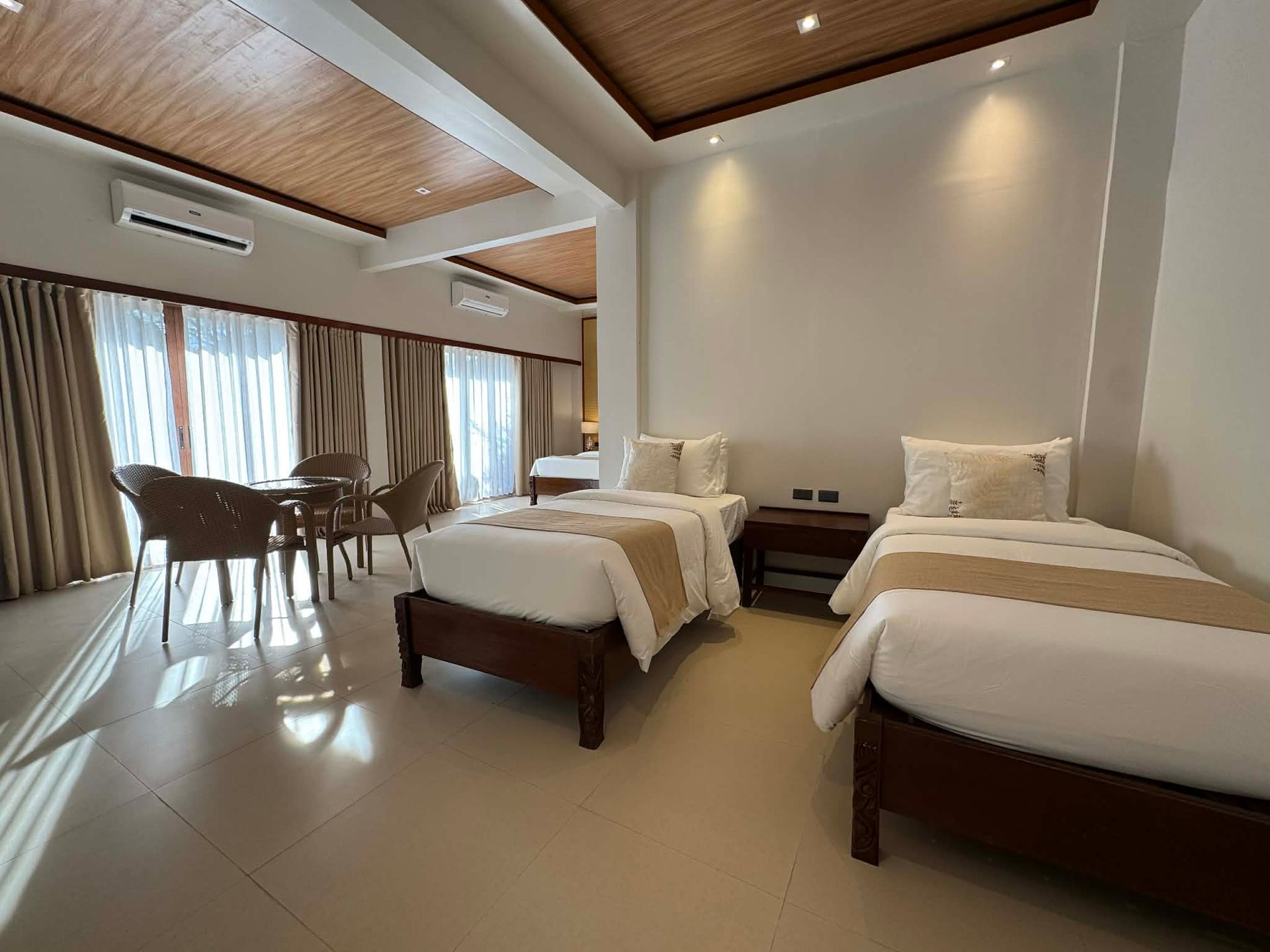 Bright modern hotel room with two twin beds, a seating area, and large windows with curtains