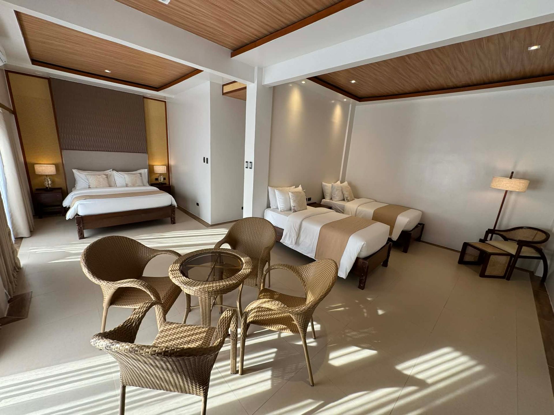 Spacious bedroom with two beds, wicker chairs, and warm wood ceiling in soft daylight