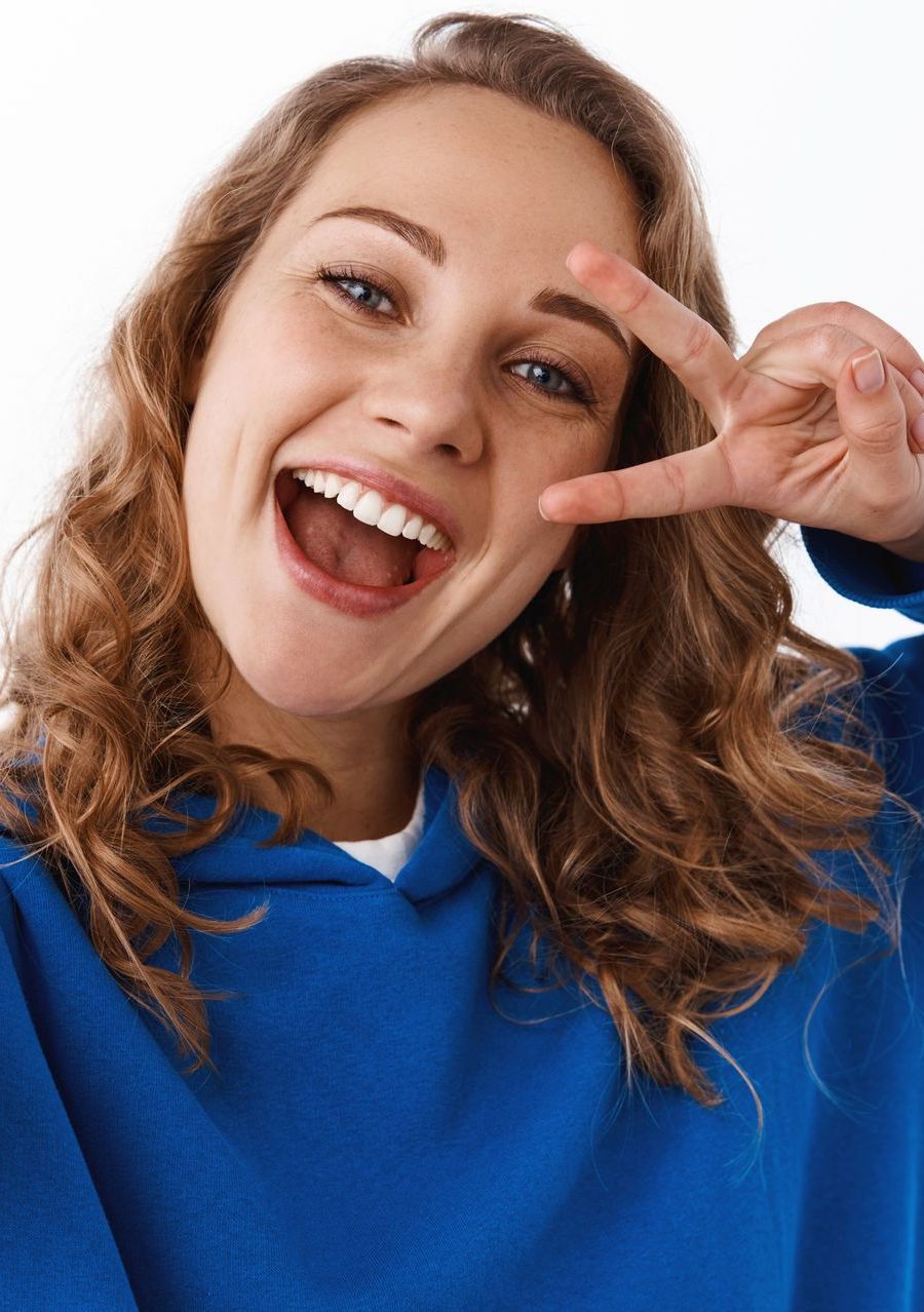 Una donna con una felpa blu sorride e fa il segno della pace - Arte Dentale Frosinone