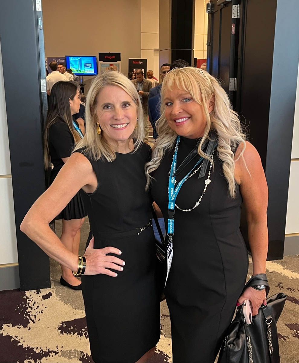 Two women in black dresses are posing for a picture