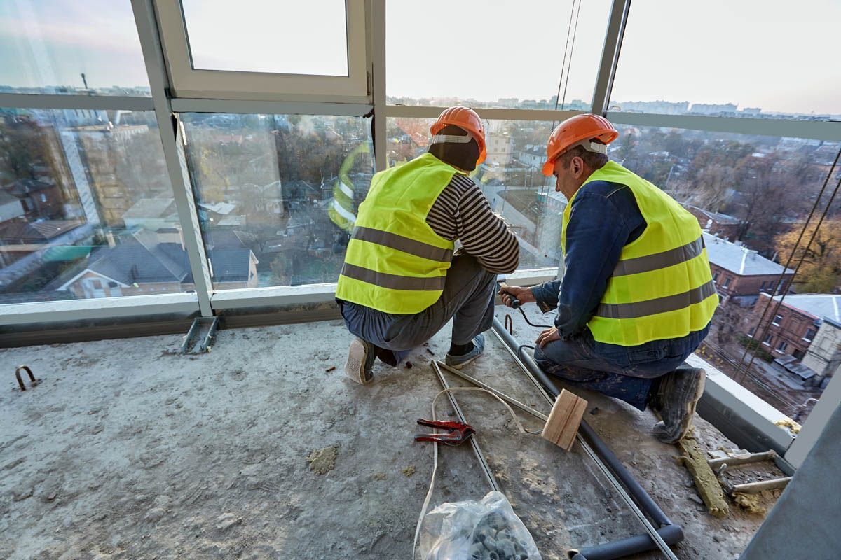 Two construction workers are working on a balcony.