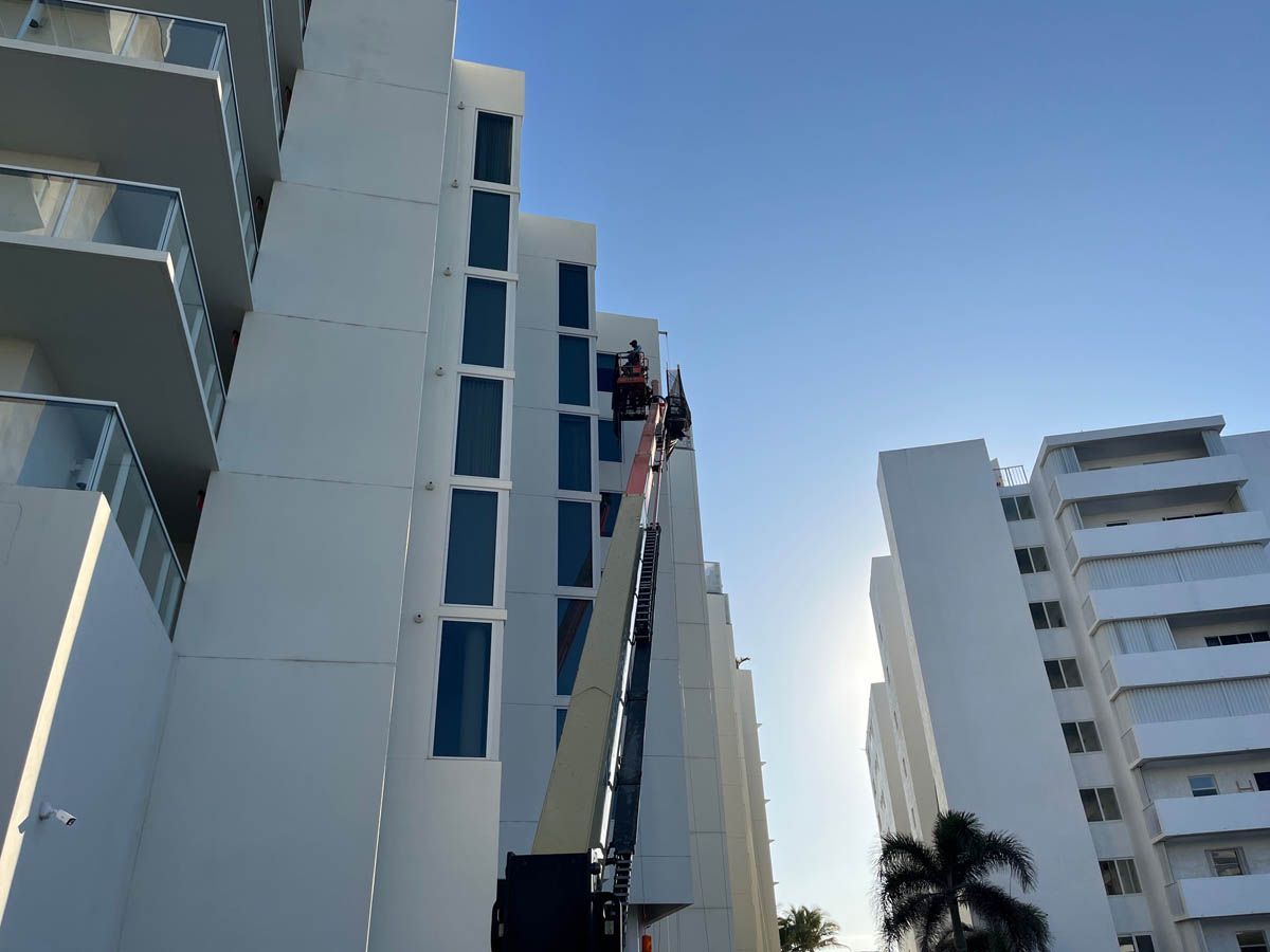 A man is standing on a crane in front of a tall building.