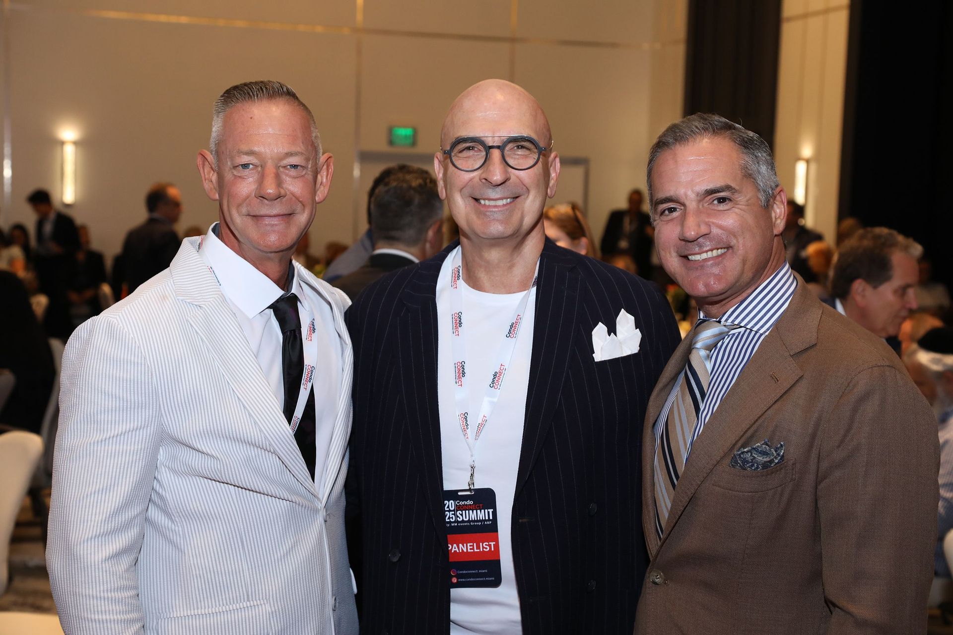 Three men smiling, posing together indoors at an event.