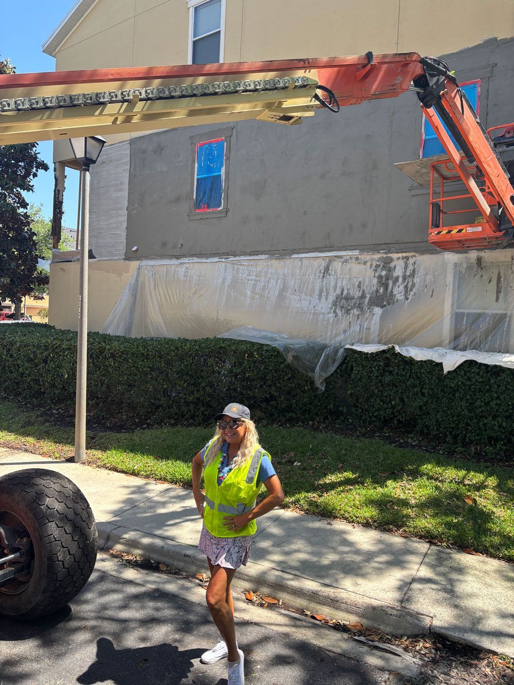 Woman in safety vest stands near construction on a building. An orange lift reaches the building’s exterior.