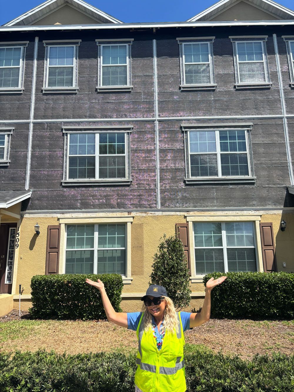 Woman in safety vest poses in front of a three-story building with weathered siding.