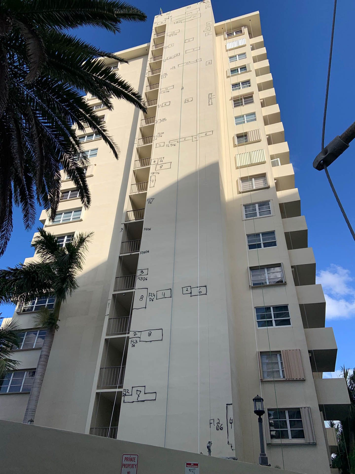 Tall beige apartment building against a blue sky, with visible balconies and windows.