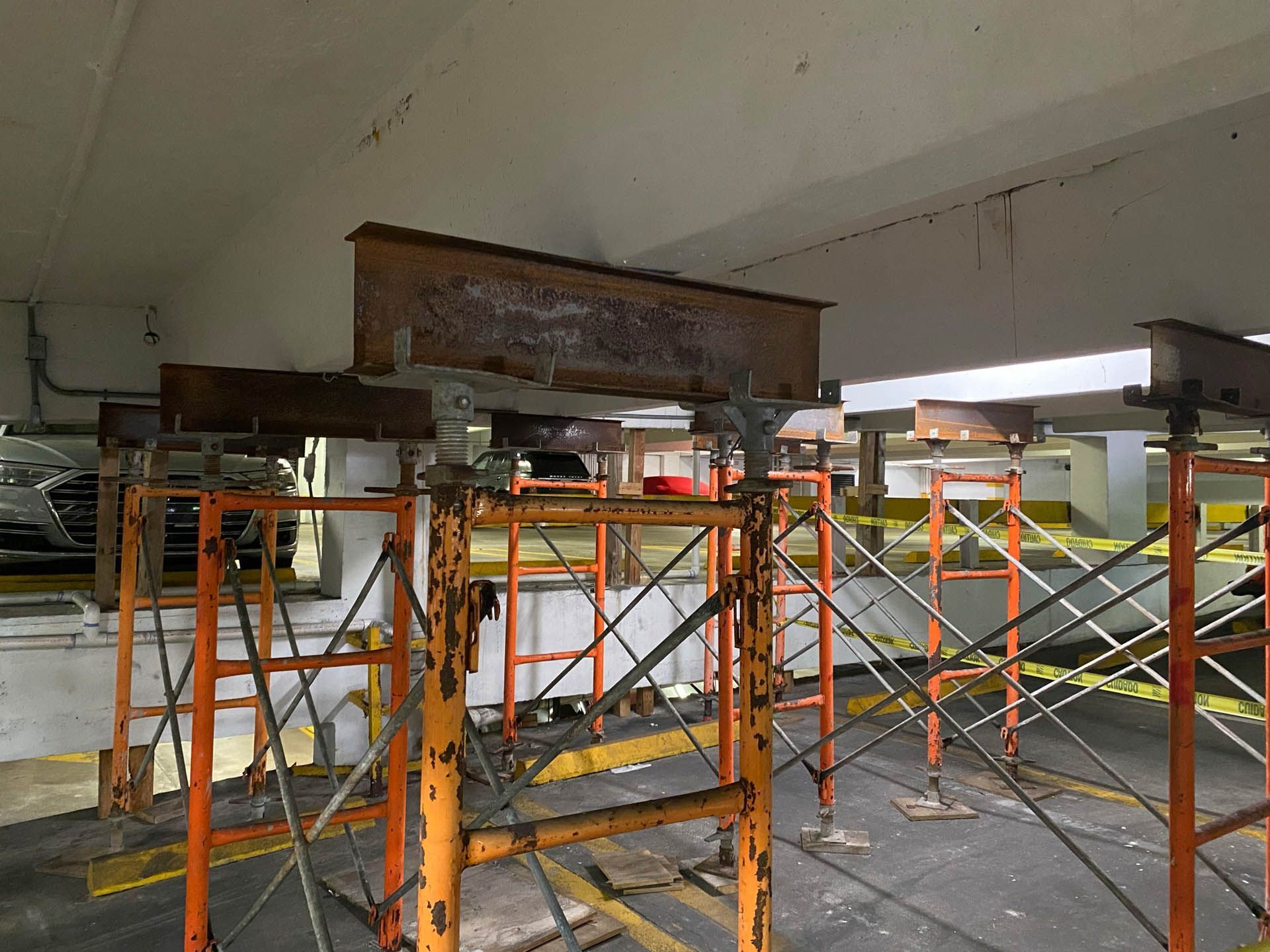 Rust-colored steel beam supported by orange scaffolding in a parking garage.
