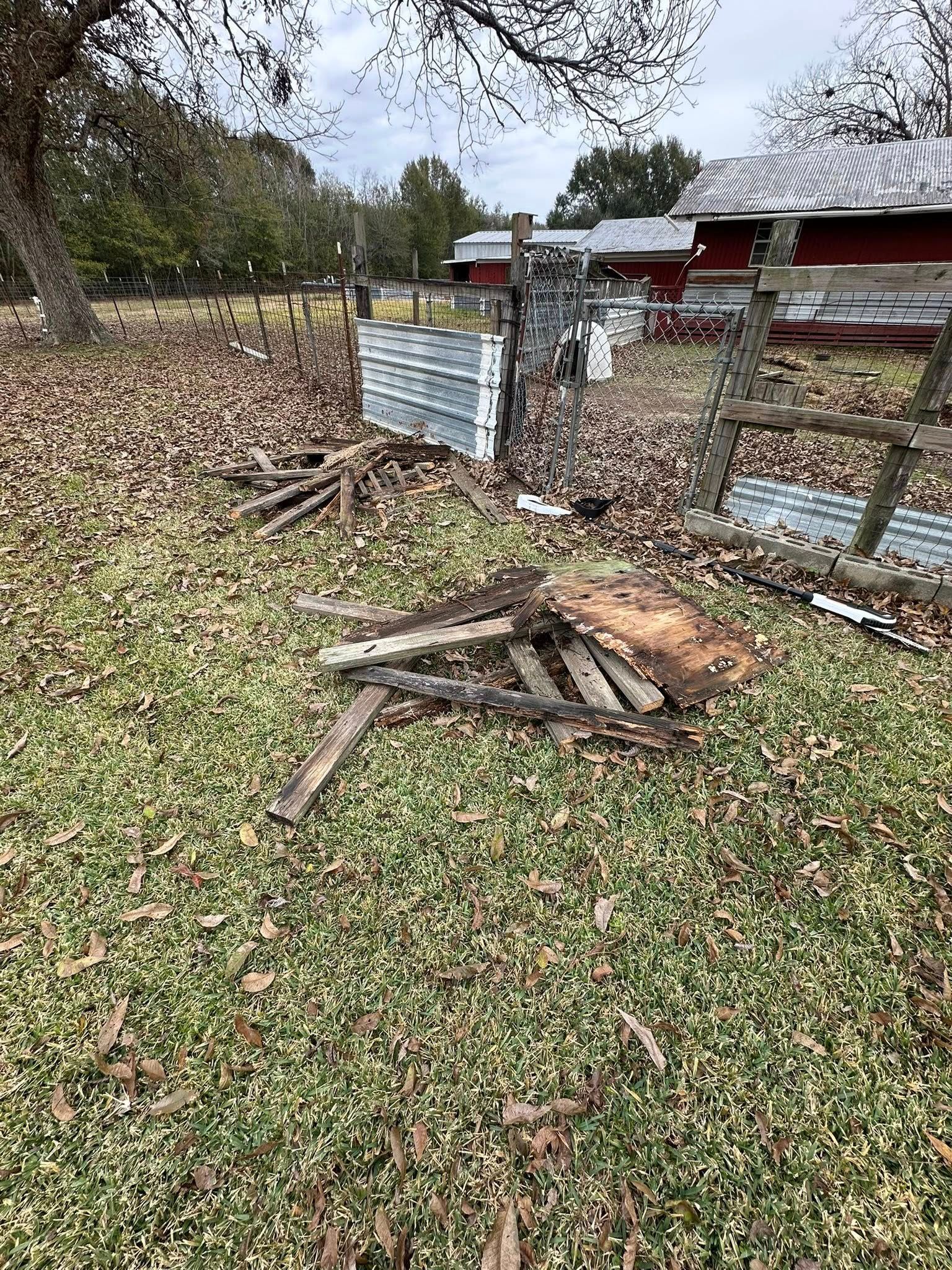 Debris, including wooden planks and a metal sheet, scattered on a lawn covered in fallen autumn leaves near a red barn.