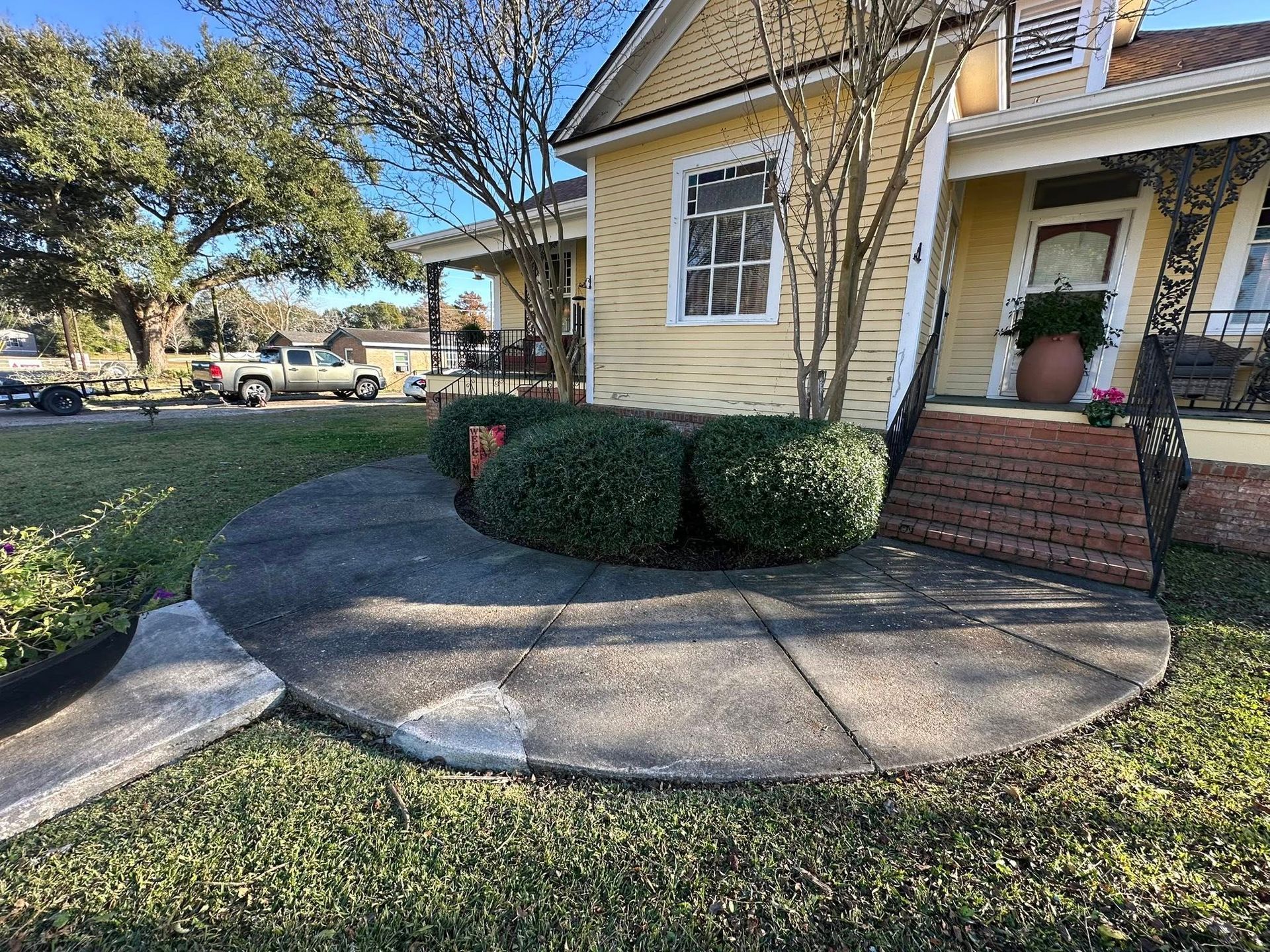 A yellow house with a semicircular concrete patio, a brick staircase, and green bushes in the front yard.