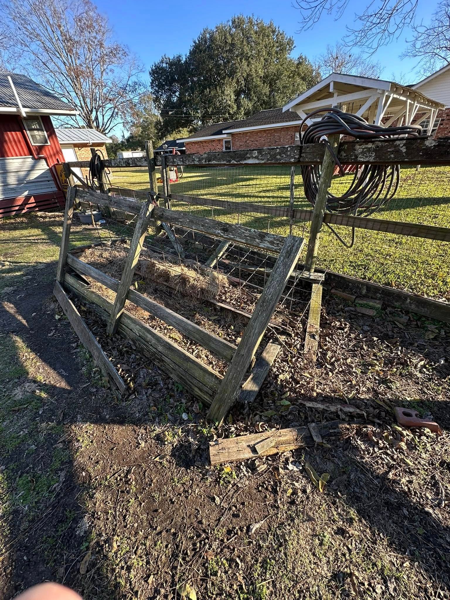 A weathered wooden trellis frame lies partially collapsed over a ground covered in brown leaves in a sunny backyard.