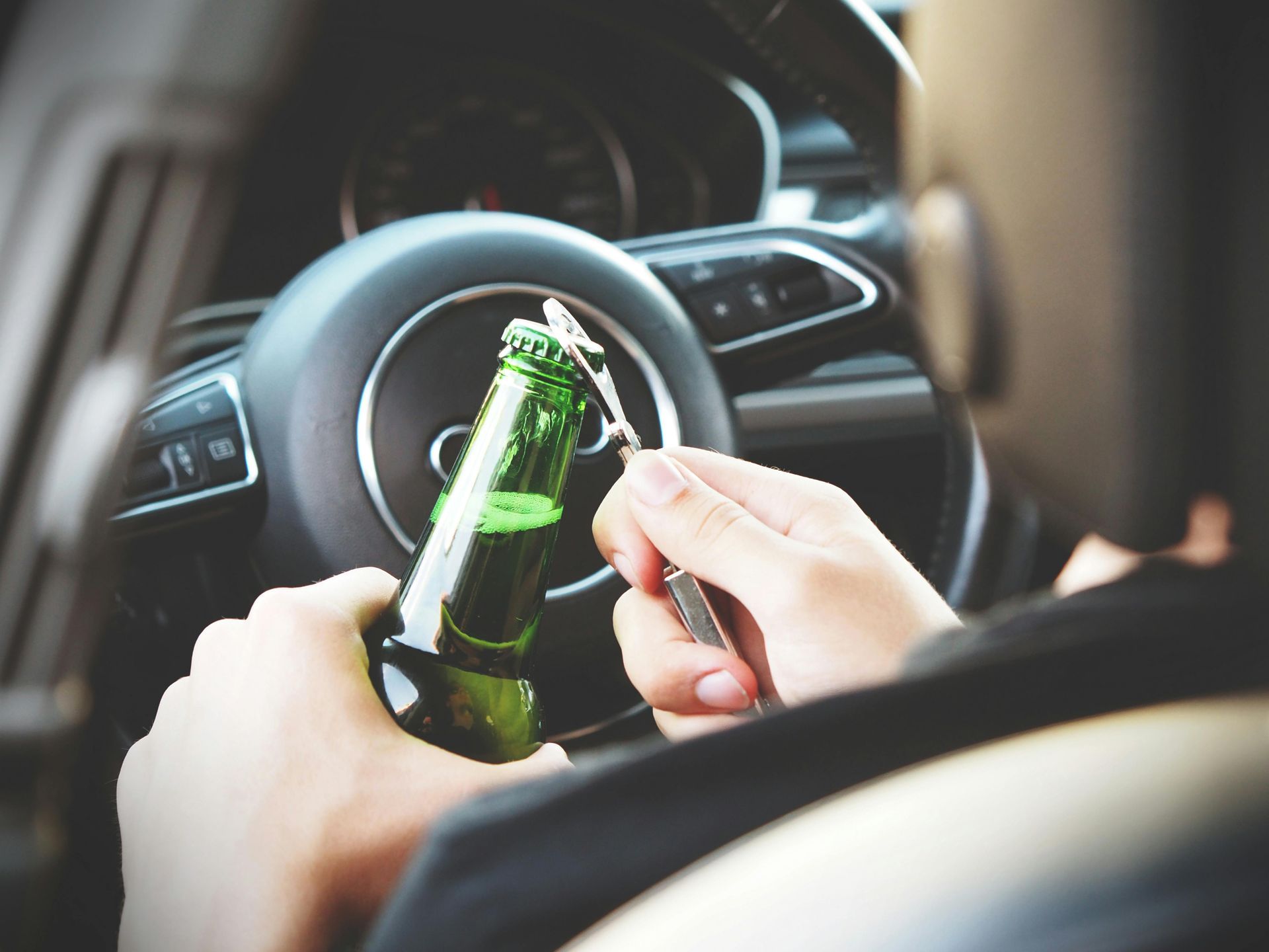 Person opens beer bottle while sitting behind the steering wheel of a car.