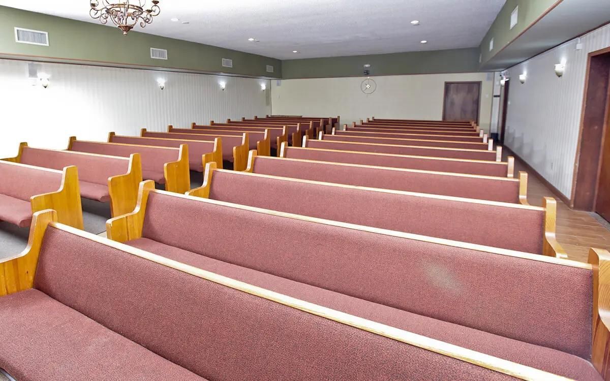 Empty chapel with rows of red-cushioned pews and a doorway.