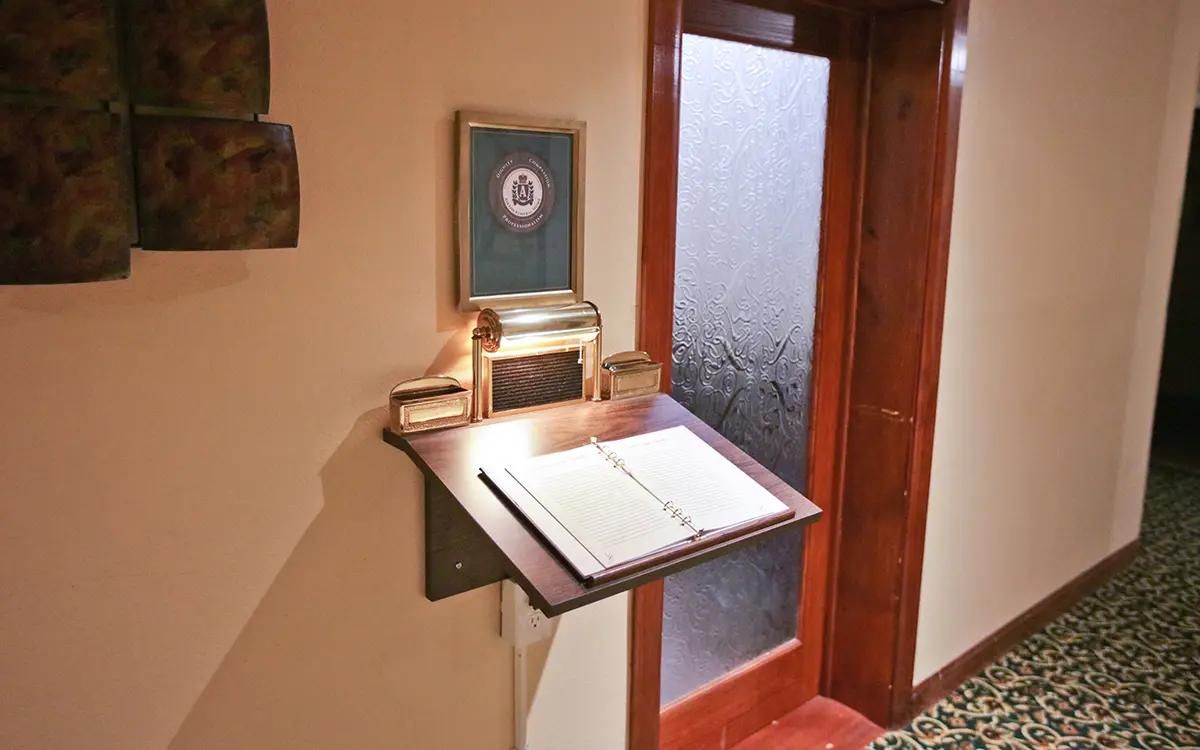 A guest book on a small table near a door. A frame and metal box are also on the table, and the wall is beige.