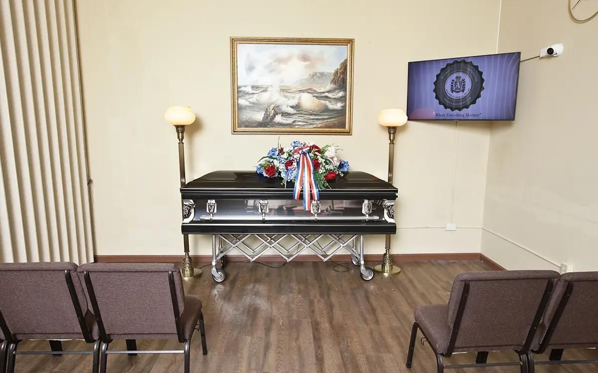 Funeral home interior with casket, floral arrangement, chairs, and artwork.
