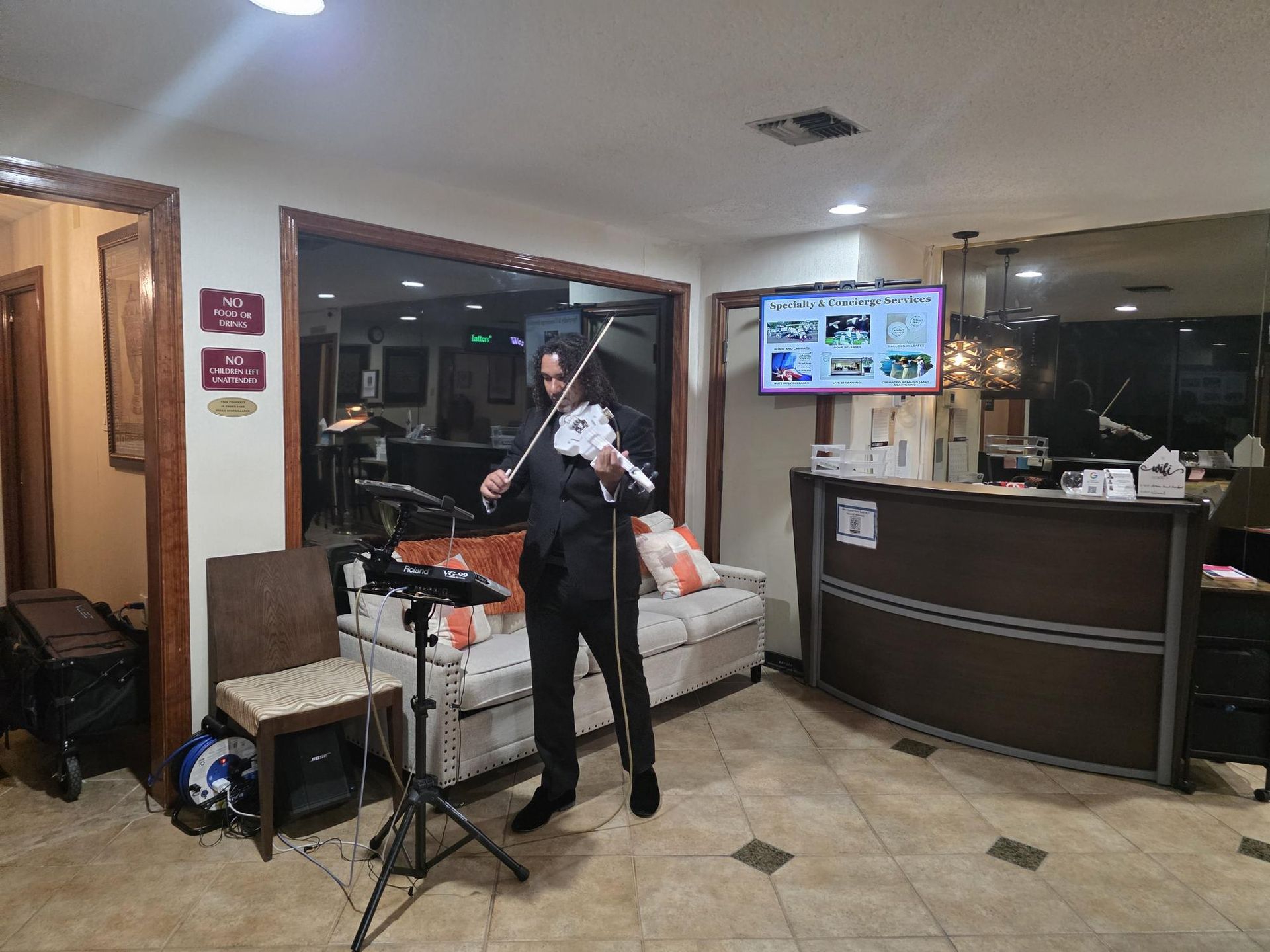 Man in black suit playing a white violin in a hotel lobby.