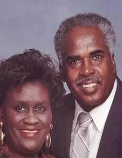 Smiling couple in formal attire, posing close together, against a plain backdrop.