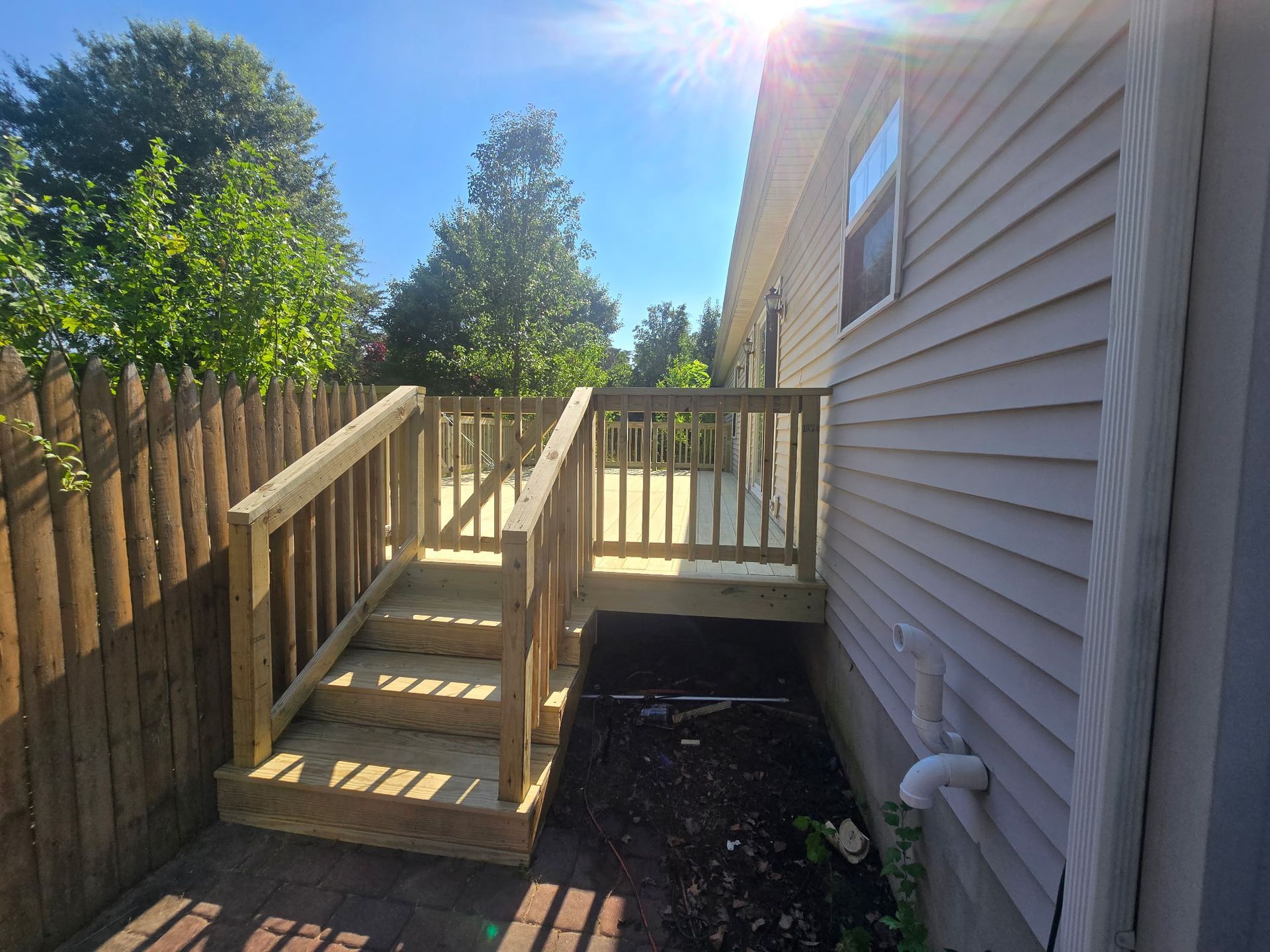 Wooden accessibility ramp with steps beside a house, leading to a backyard deck in bright sunlight