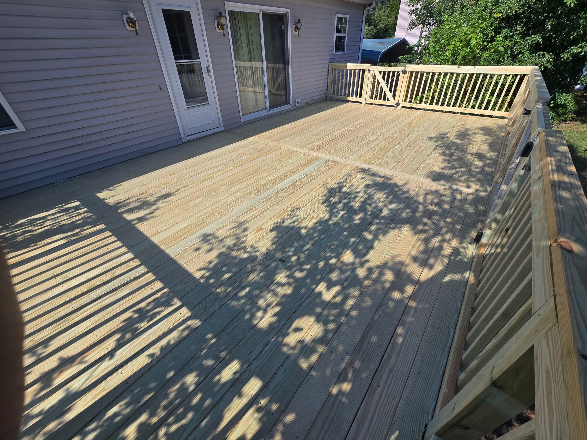 Wooden deck beside a house with beige railings and tree shadows in sunlight