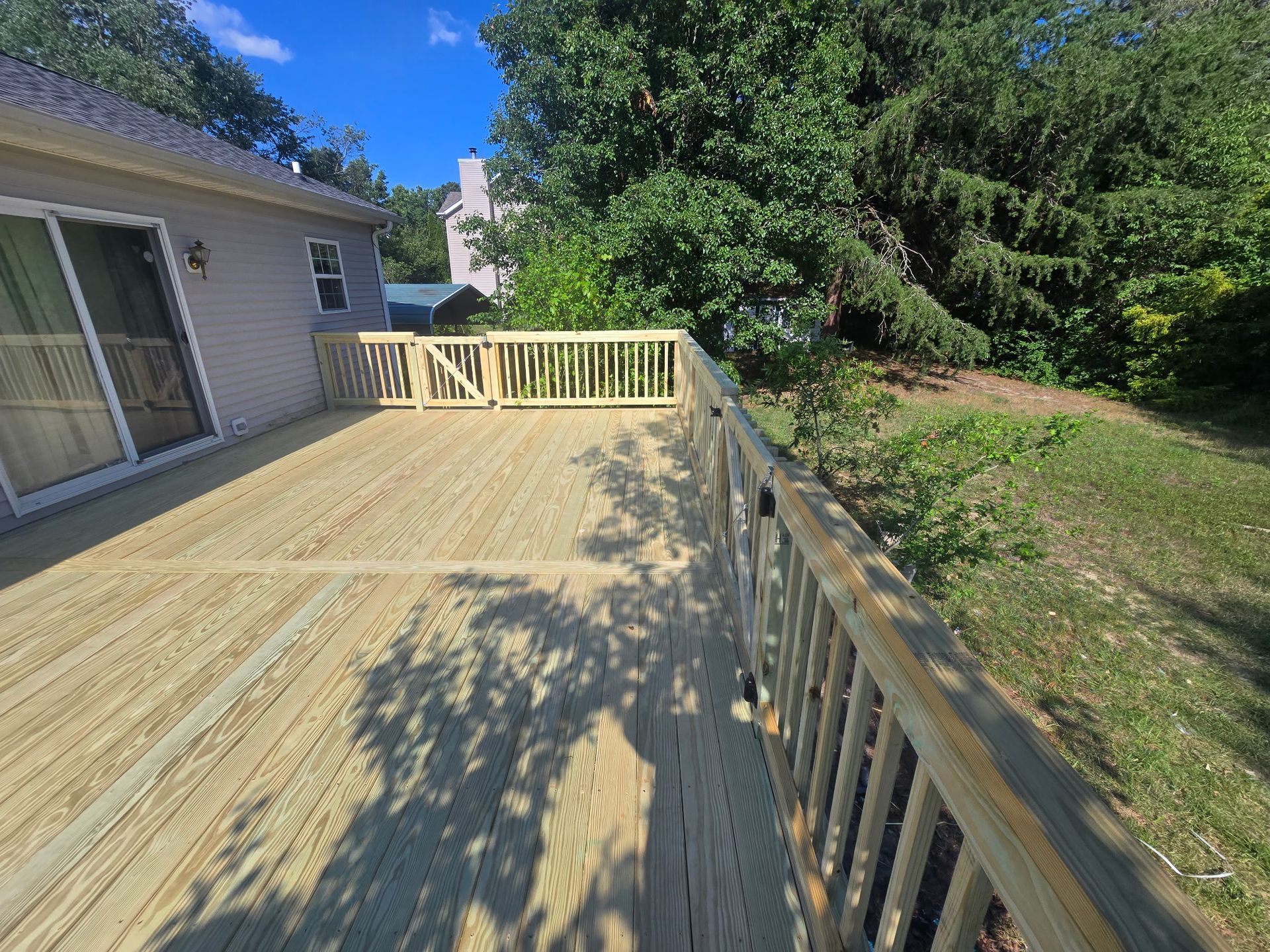 Wooden deck beside a house, with railings and a view of trees and grassy yard.