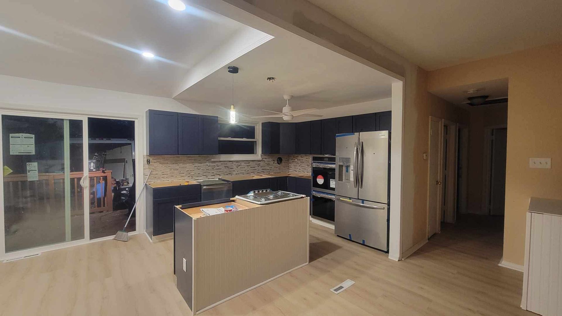 Modern kitchen and living area with island, dark cabinets, stainless fridge, and sliding glass doors
