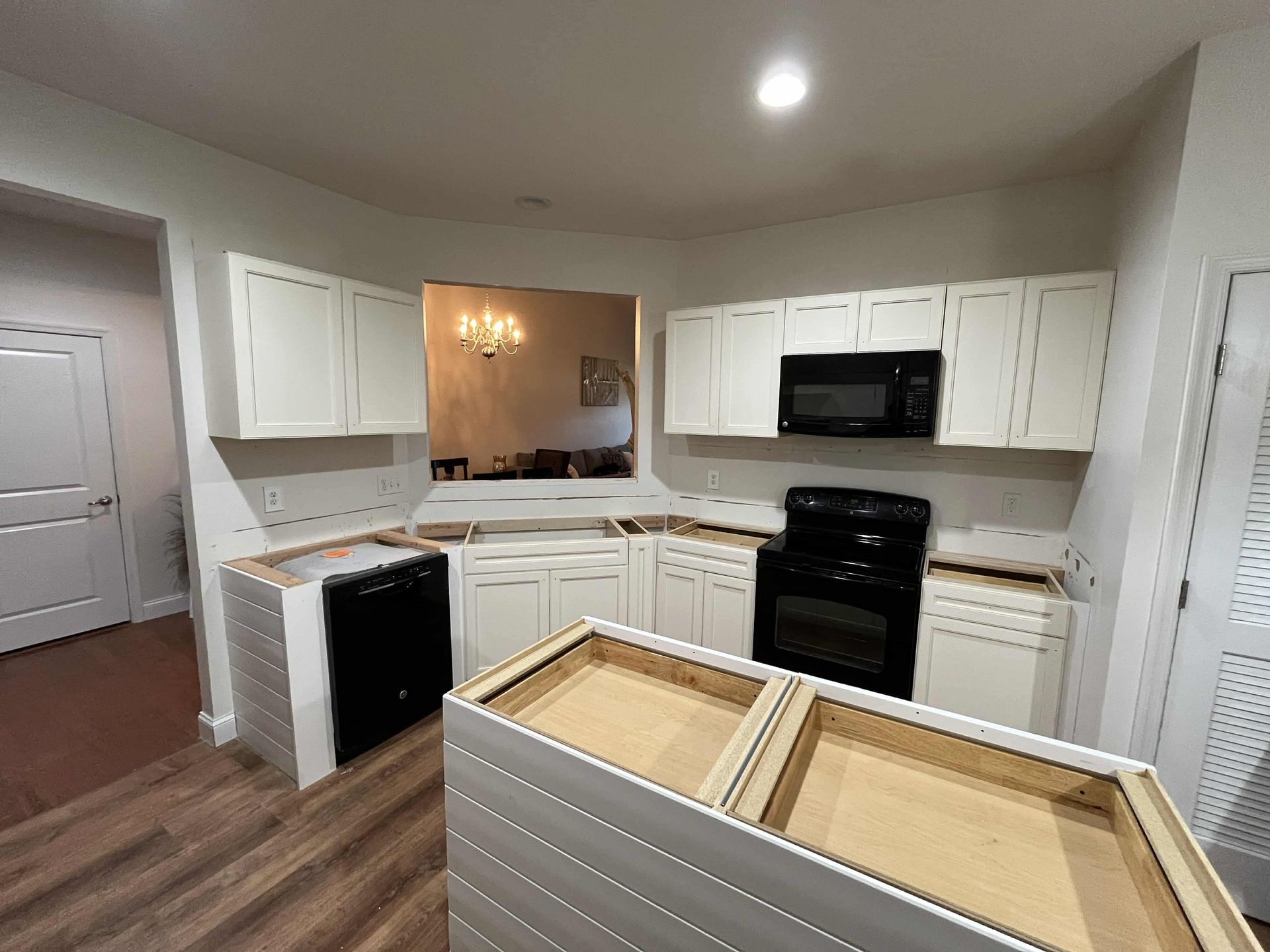 Modern white kitchen with black appliances and a wood-floored island under construction