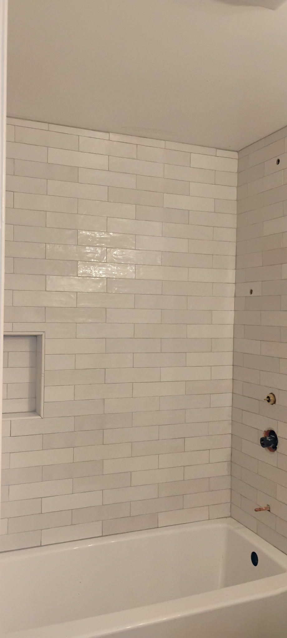 White subway-tile bathroom shower/tub with built-in niche and black fixtures