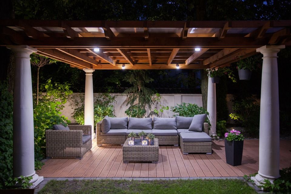 Patio seating under a pergola with overhead lighting, in a garden at night.