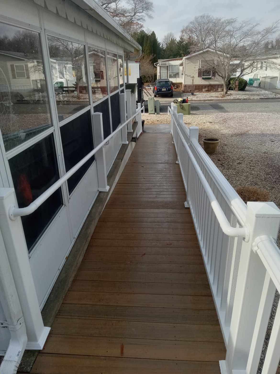 Wooden wheelchair ramp with white railings beside a house and pebbled yard on a cloudy day