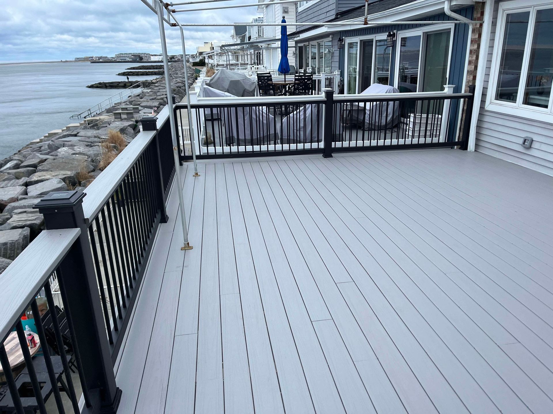 Deck overlooking rocky waterfront with black railing and white house siding beside calm water