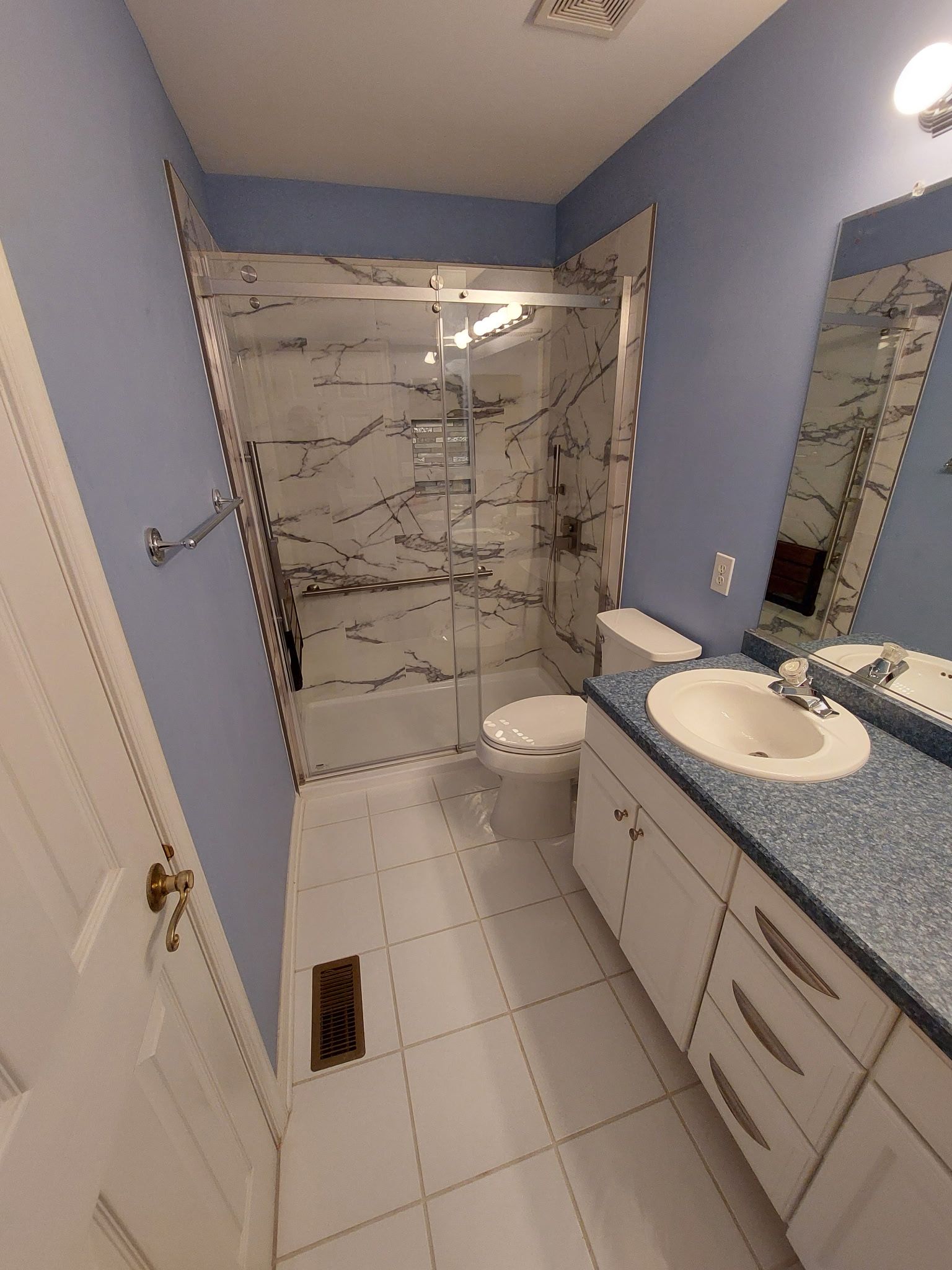 Small bathroom with white tile, blue walls, glass shower, vanity sink, and mirror.