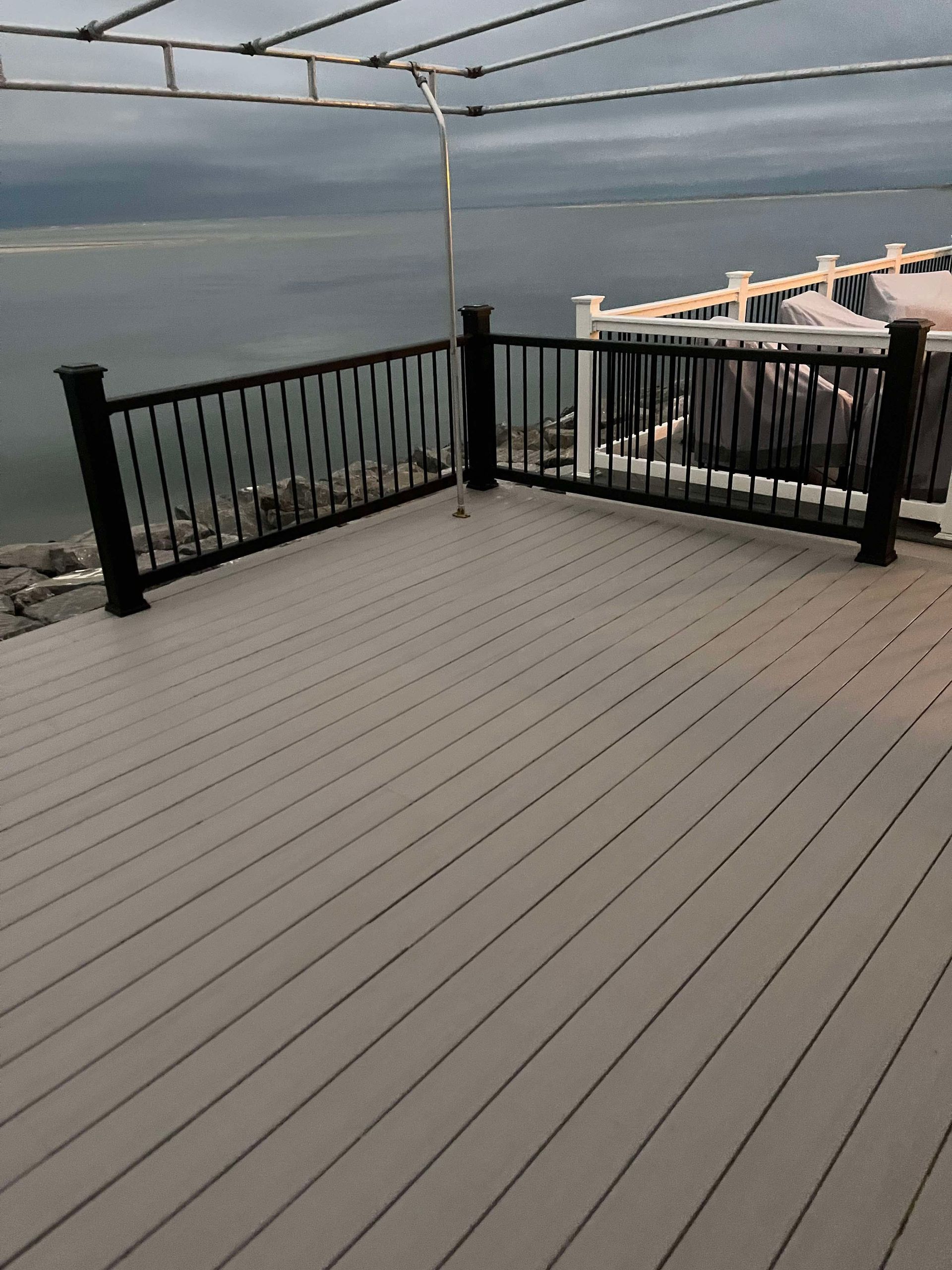 Wooden deck overlooking a calm body of water, with black railings and an overcast sky.