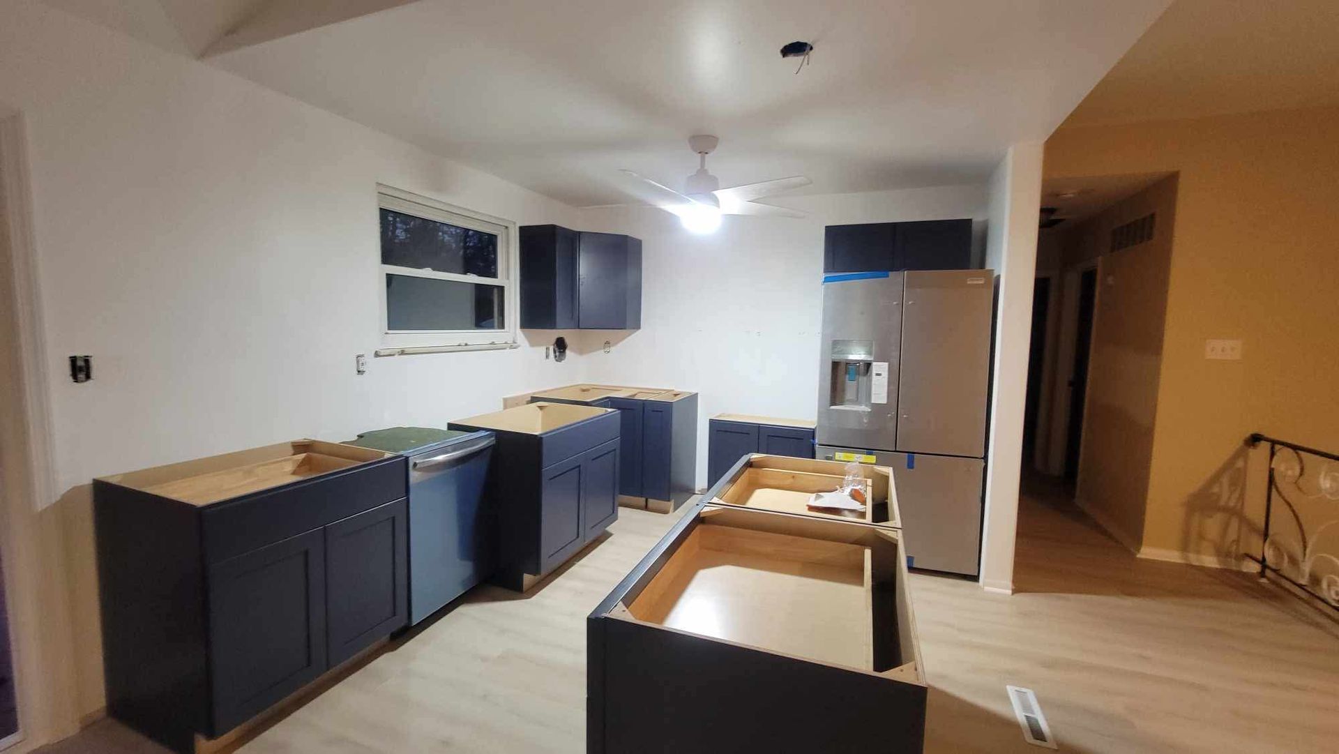 Unfinished kitchen with dark cabinets, white appliances, and a ceiling fan in a bright room.