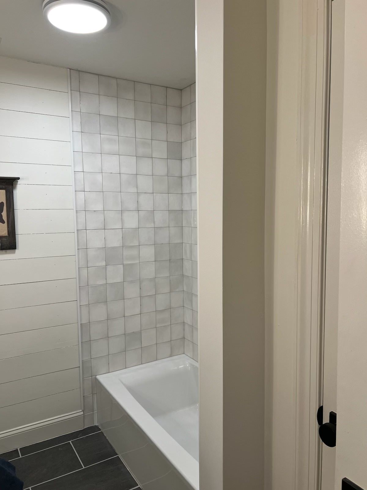 Small bathroom with white tiled walls and a bathtub corner.
