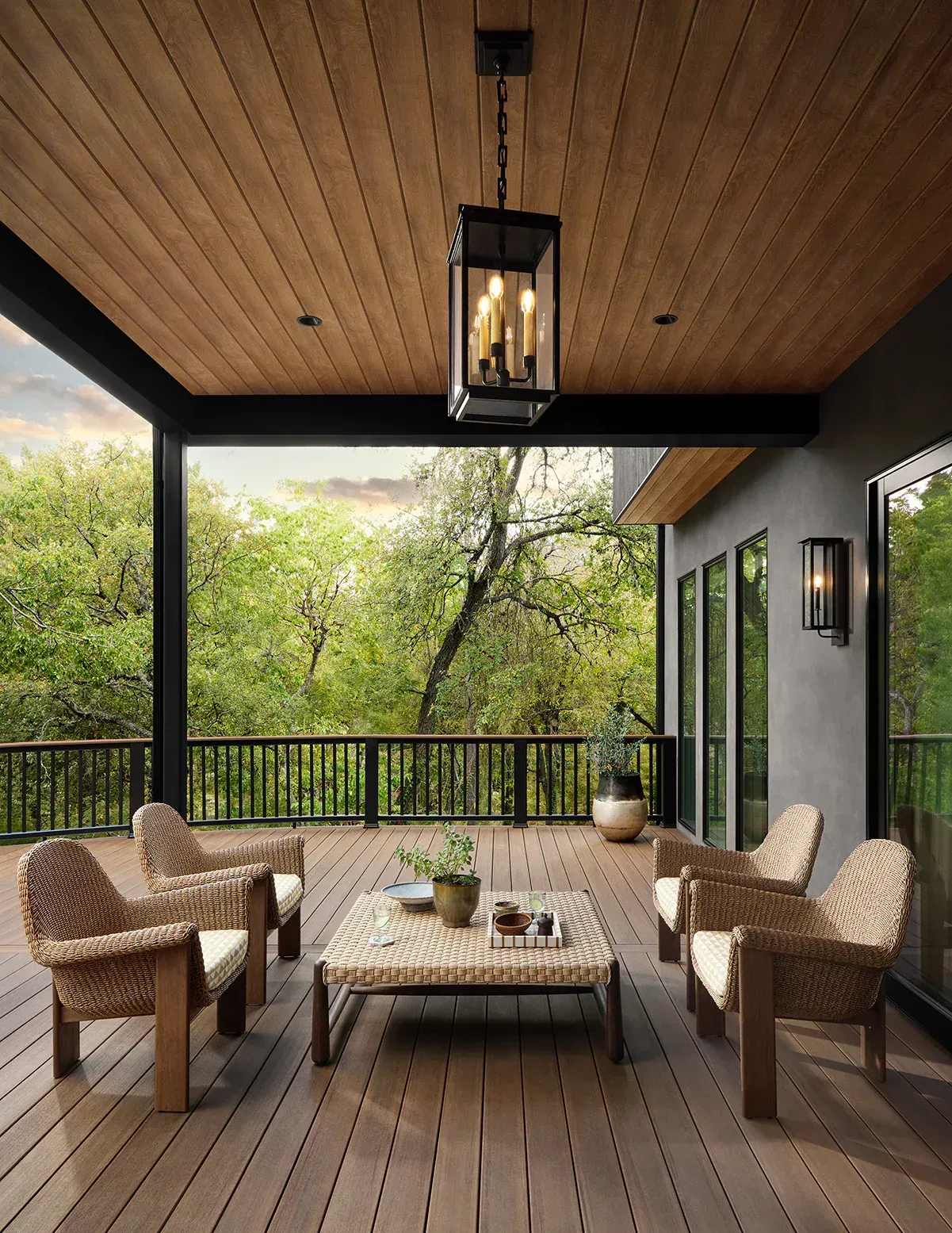 Covered patio with woven chairs and a coffee table overlooking lush green trees