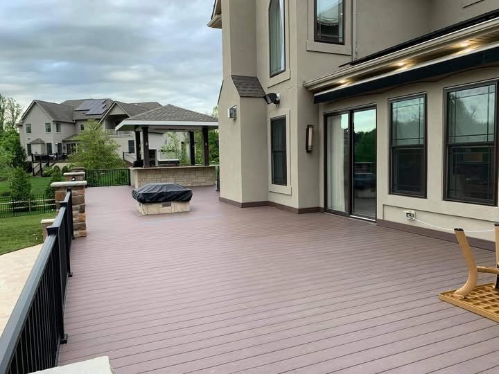 Spacious backyard deck with black railing, beige siding, and a hot tub in a suburban neighborhood.