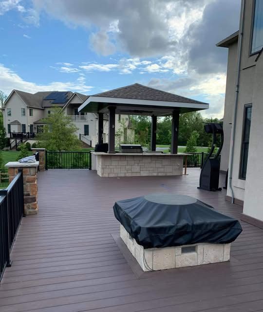 Backyard deck with covered outdoor kitchen, stone seating, and gray bench under a cloudy sky