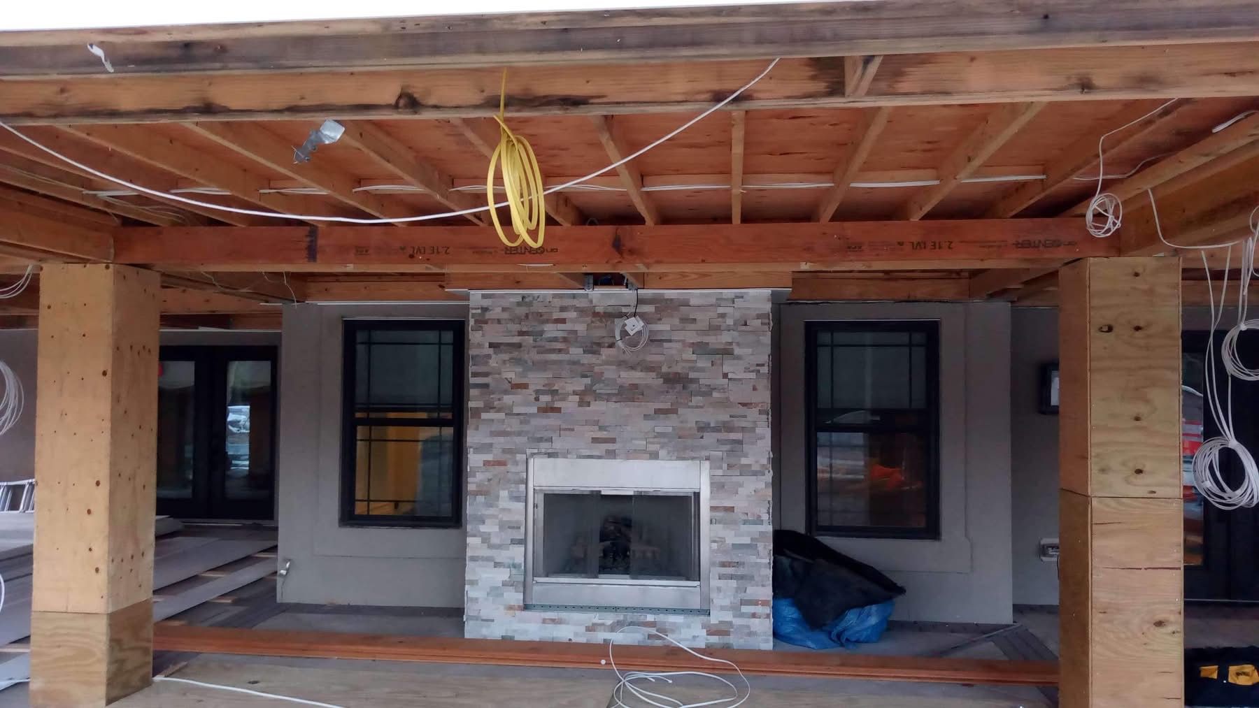 Covered patio with stone fireplace, wooden beams, and two windows beside it.