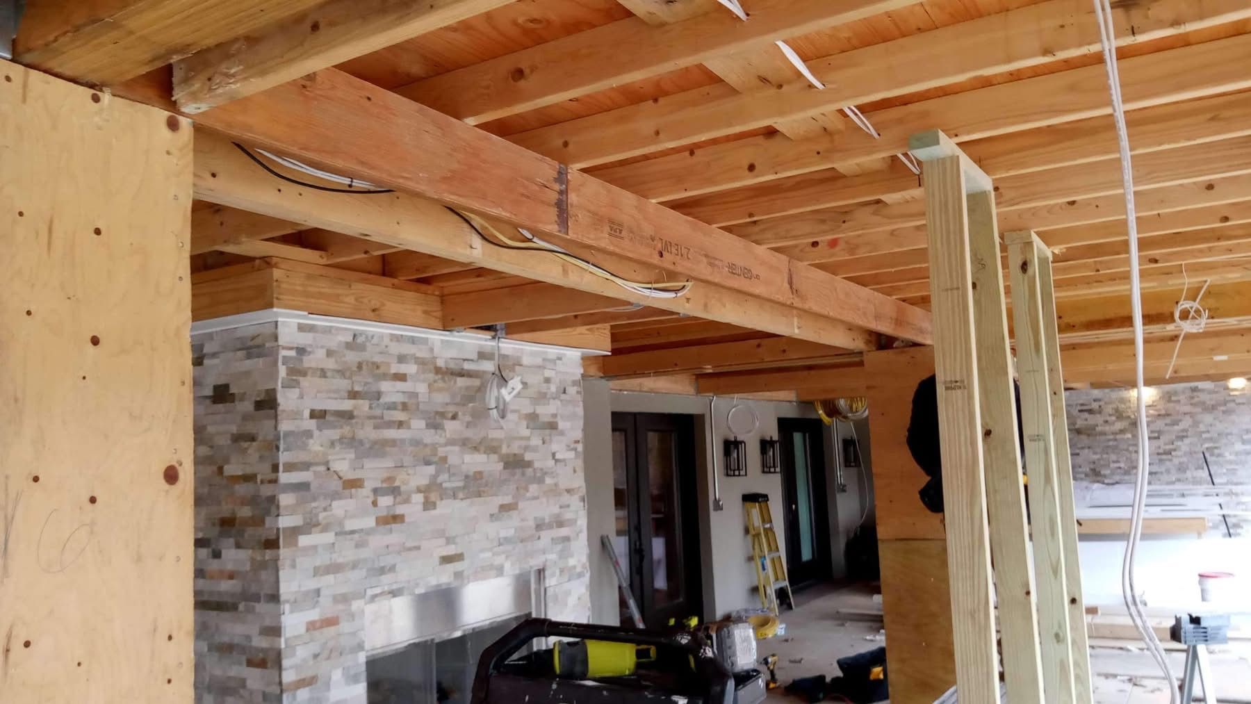 Interior under renovation with exposed wooden ceiling joists, stone accent wall, and construction materials.