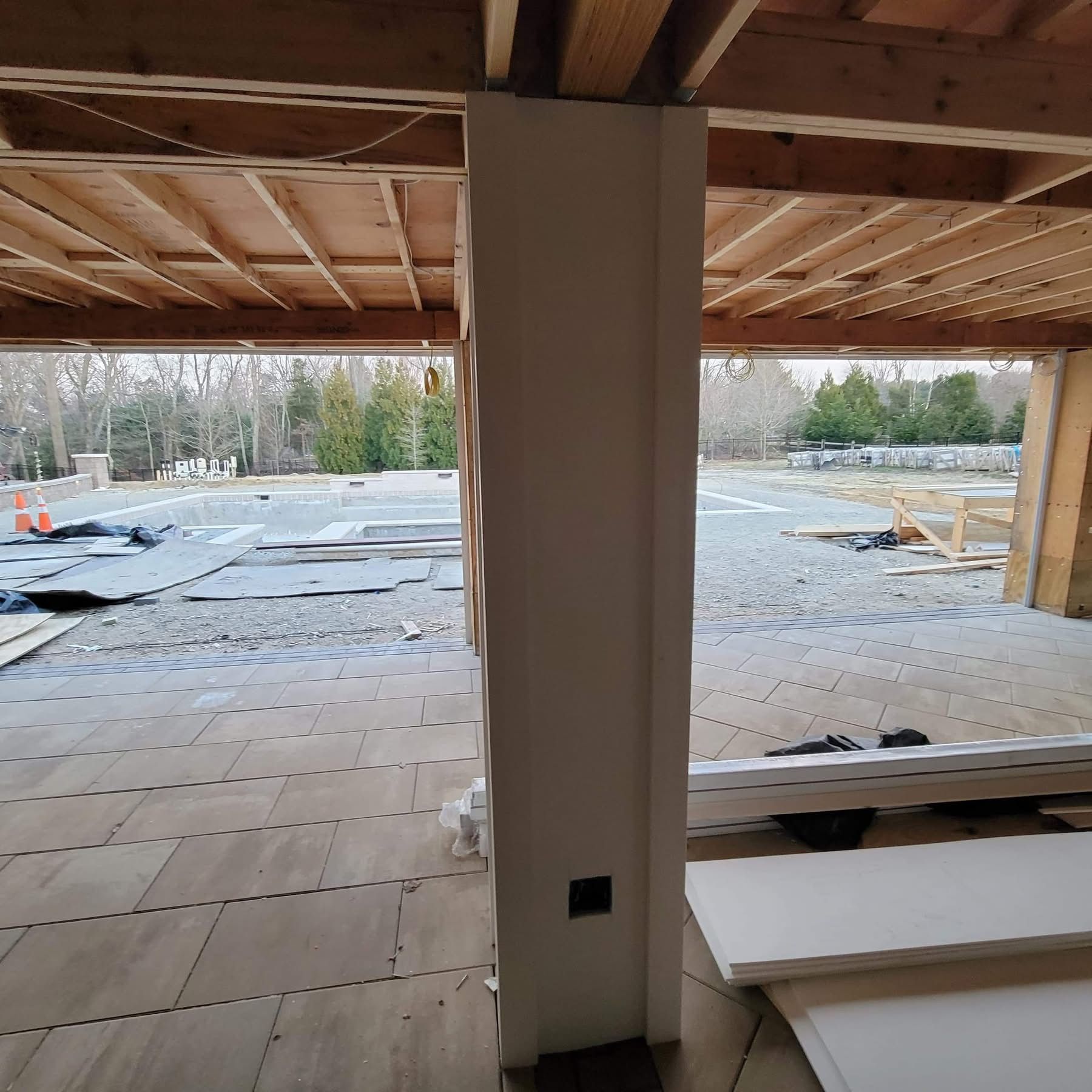 Unfinished interior with exposed wood framing, central column, and view of snow-covered ground outside.