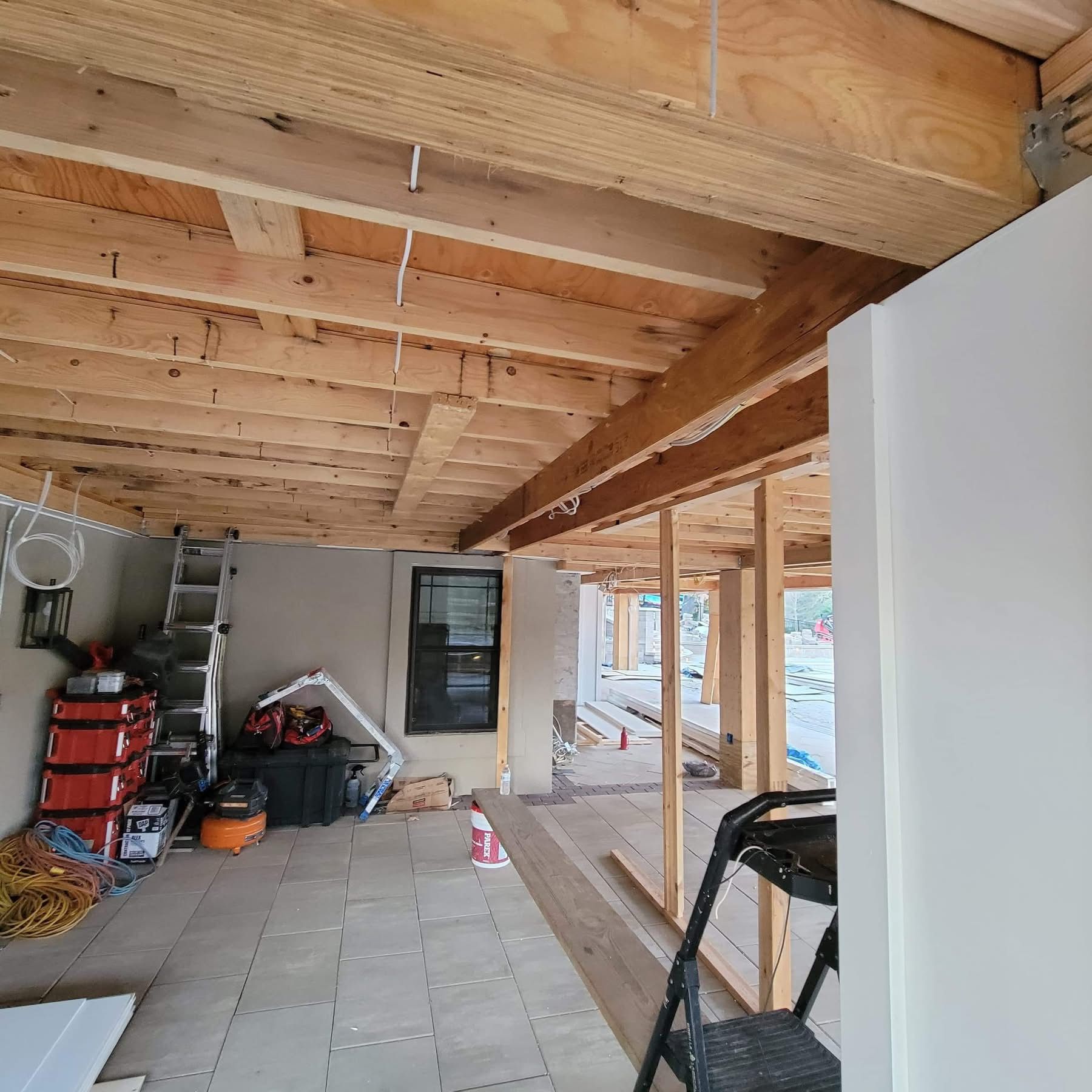 Covered patio or garage interior with exposed wood beams, tiled floor, storage shelves, and an open side view outdoors