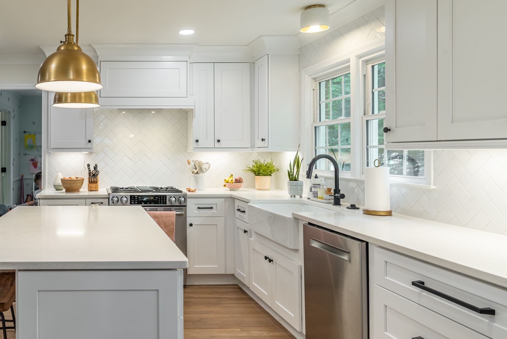 Bright white modern kitchen with brass pendant lights, island, and stainless-steel appliances