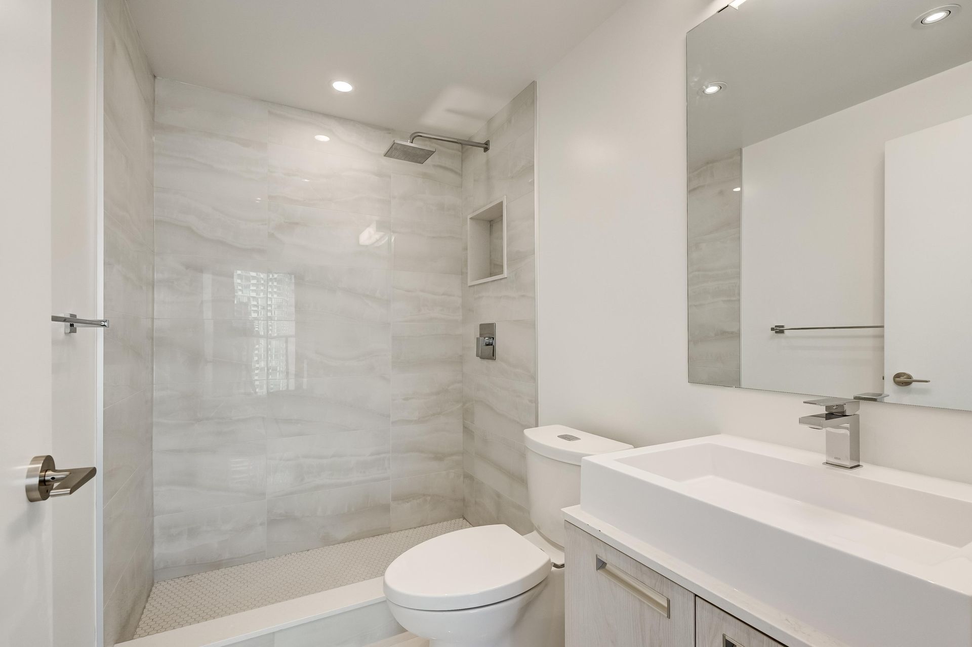 Modern white bathroom with walk-in shower, toilet, and vanity sink.