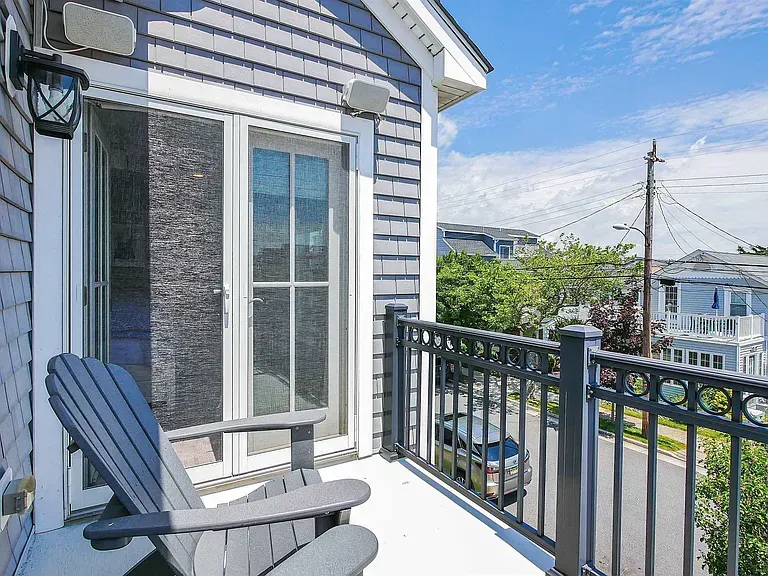 Balcony with gray chair, sliding glass door, and black railing overlooking a residential street