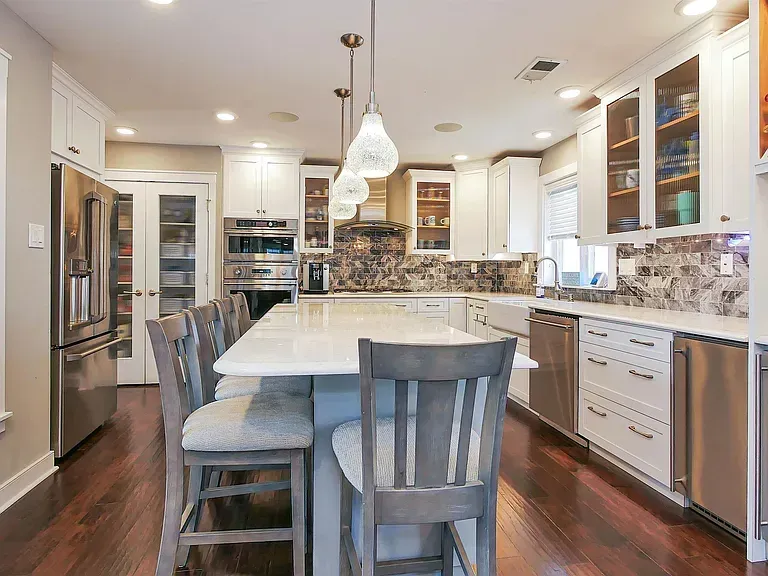Bright modern kitchen with white island, gray stools, pendant lights, stainless appliances, and wood floors