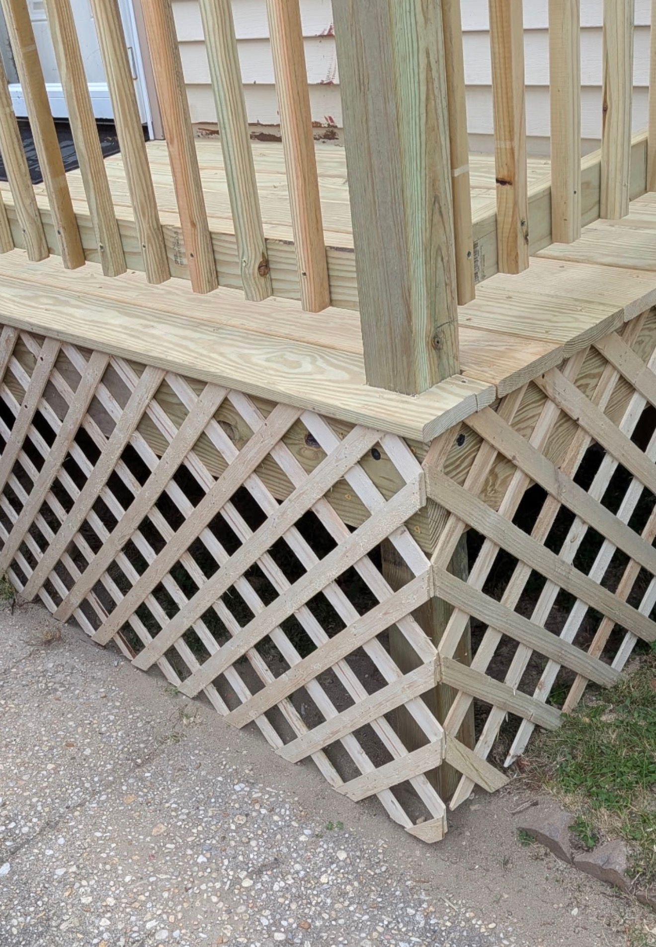 White lattice skirting under a wooden deck corner beside a concrete path and grass