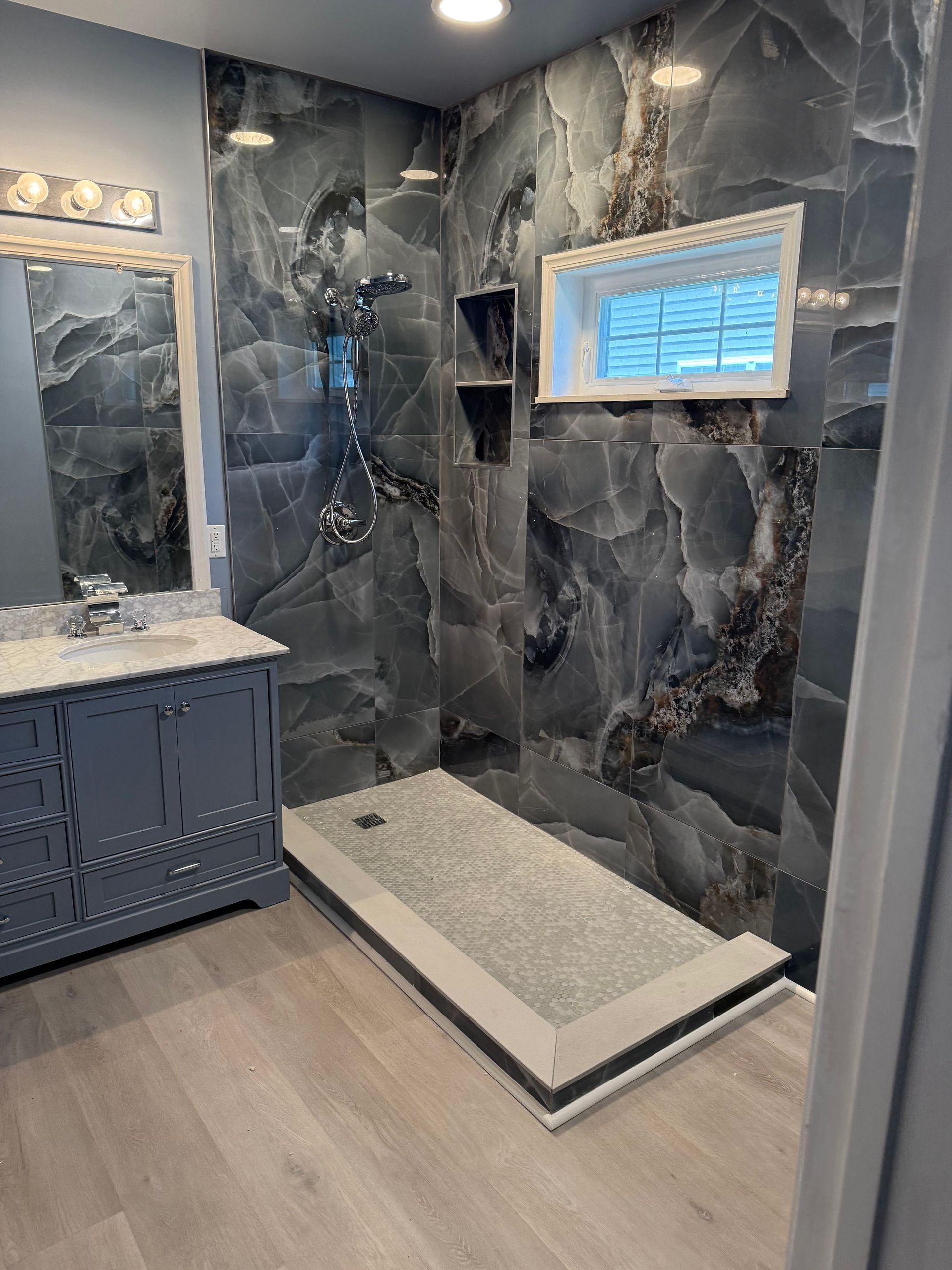 Modern bathroom with dark marble tile, white shower bench, vanity, and small window