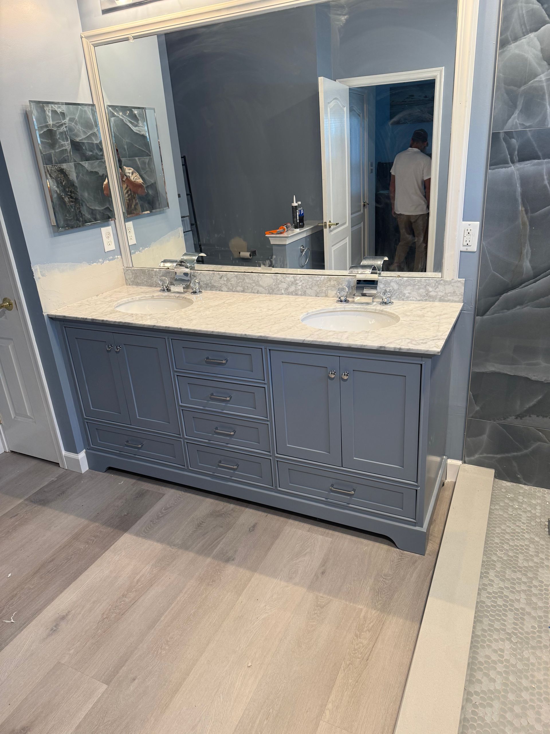 Blue bathroom vanity with double mirrors, white countertop, and gray flooring.
