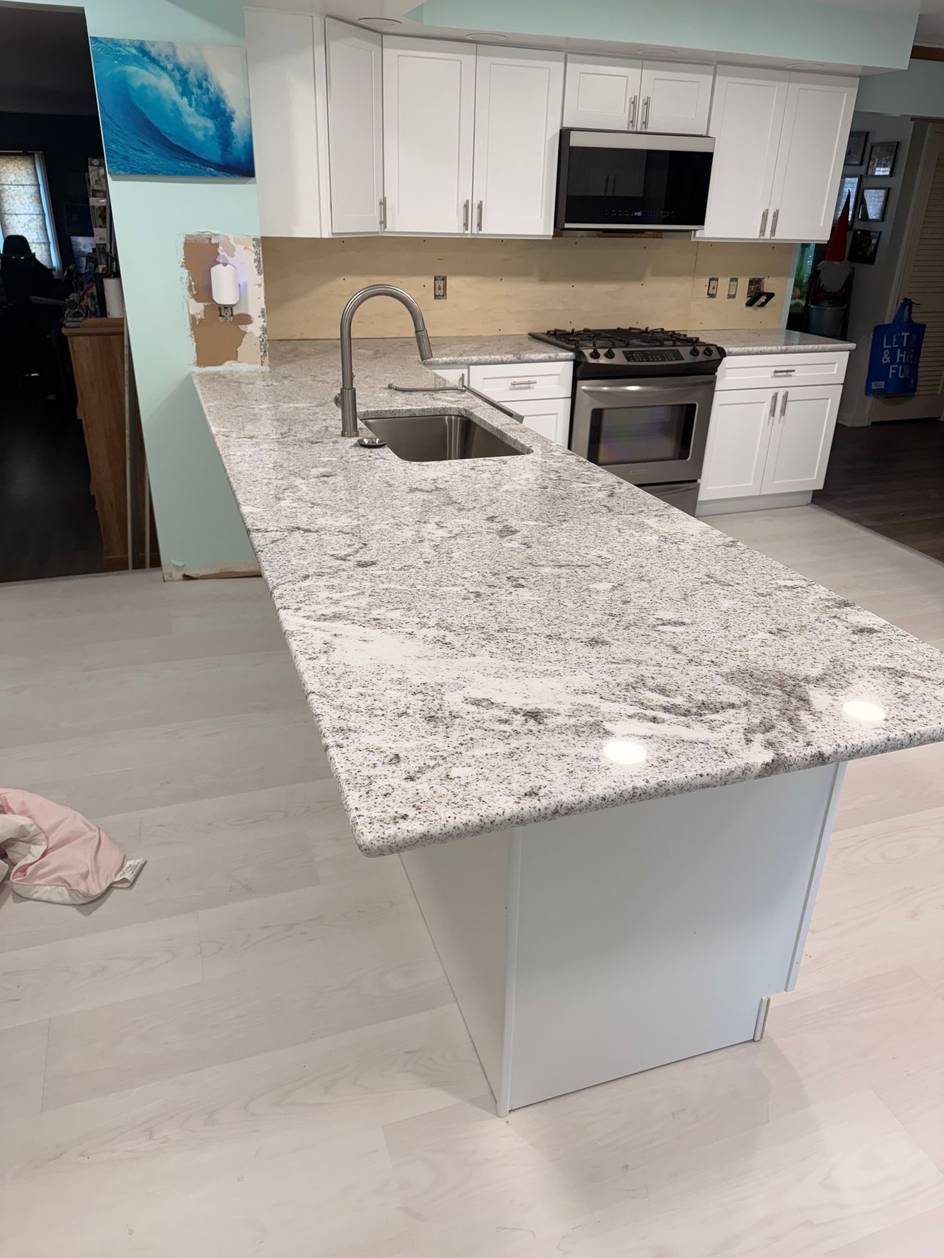 Modern kitchen with white cabinets, granite island, stainless sink, and gas stove.